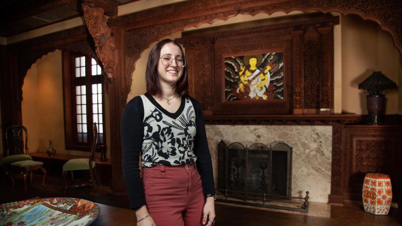 Melanie Shefchik stands in the Teakwood Room with the fireplace behind her.