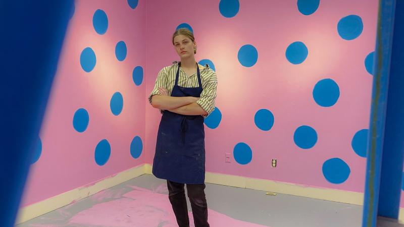 Charlie Wetzel poses for a photo in the middle of a pink and blue art installation.