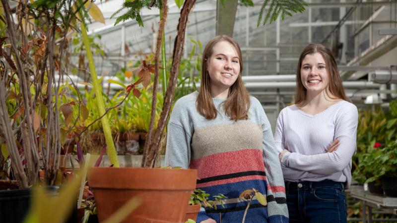 Amber Newman and Madeline Taylor stand in the greenhouse in Briggs Hall.
