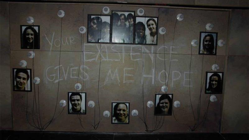 Final scene in performance "Show Your Face(s): A Masque" where students wrote the words "Your Existence Gives Me Hope" on the wall with images of students surroundings the words.
