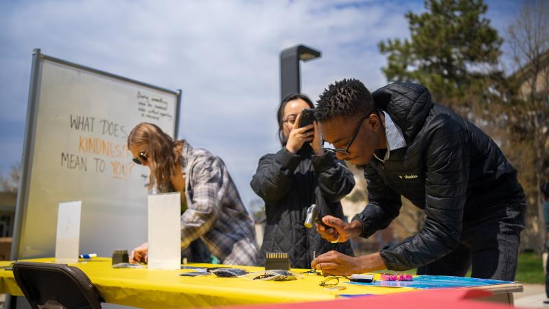 Senior Malcolm Davis joins other students at a table, making intention bracelets on the opening day of 17 Days of Kindness.