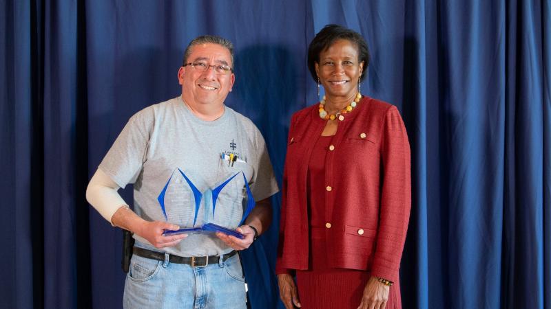 Bob Guzman holds his two awards as he poses for a photo with President Laurie Carter.