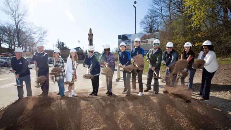 President Laurie Carter leads a group of 11 staff and students in throwing shovels of dirt at the groundbreaking ceremony.