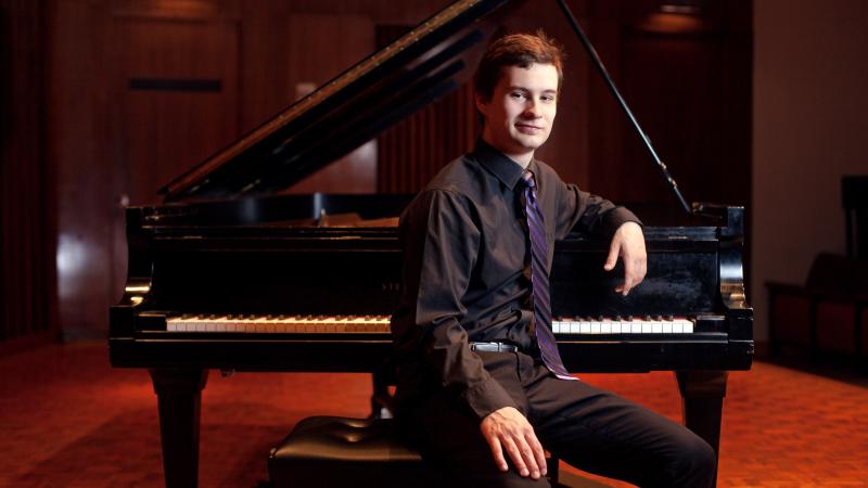 Jonathan Bass poses for a portrait in front of a piano in the Music-Drama Center.