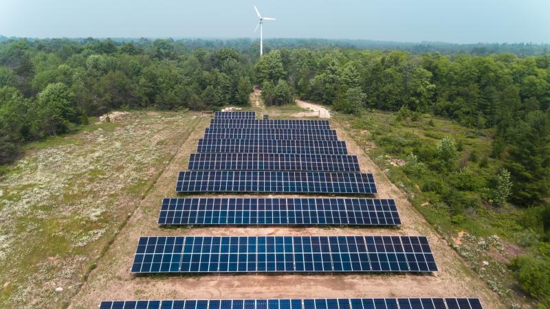 Solar panels are seen from above, with the wind turbine in the background at Bjorklunden.
