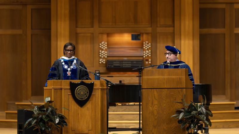 President Laurie A. Carter speaks at a podium on the stage of Memorial Chapel as Provost Peter Blitstein, at a second podium, looks on.