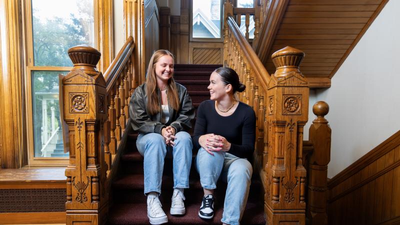 Emma Vasconez and Sydney Seeley talk on the stairs inside Lawrence's International House.