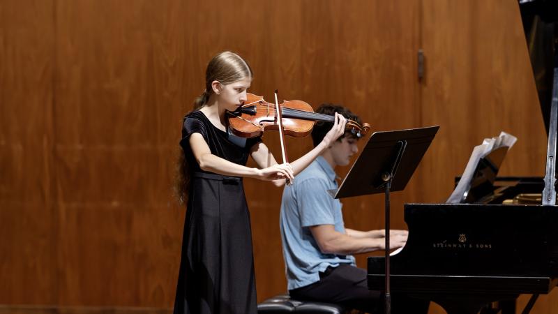 Female high school student playing violin with male student accompanying her on piano