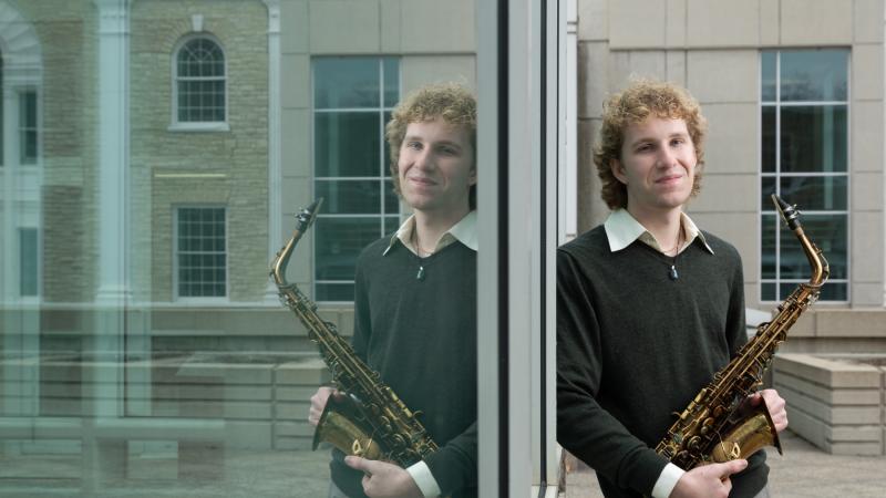 Owen Brady, holding his saxophone, is reflected in the window of Shattuck Hall.