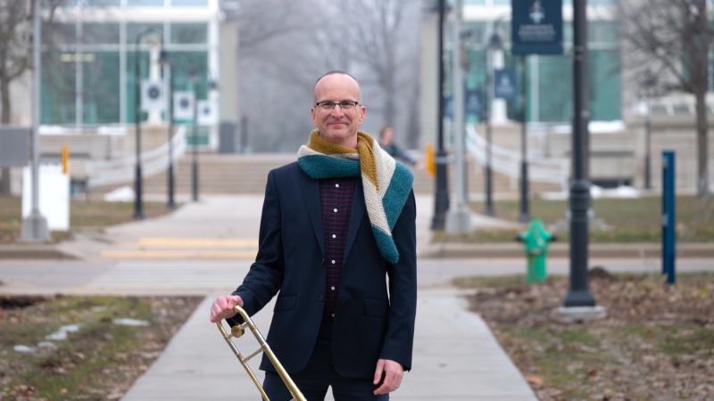 Tim Albright poses with his trombone on the sidewalk of Main Hall Green.