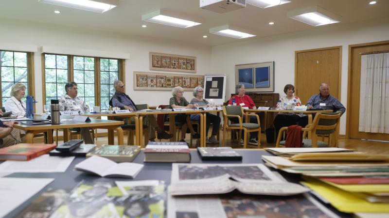 a table in the foreground with paper and students in the background