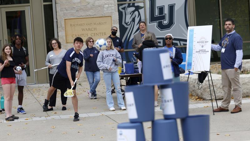 Students use lacrosse sticks to knock down cups to win prizes during Giving Day activities outside of Warch Center.