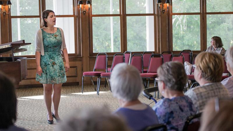 Student singing for elderly crowd at Riverview Gardens during a Music for All performance