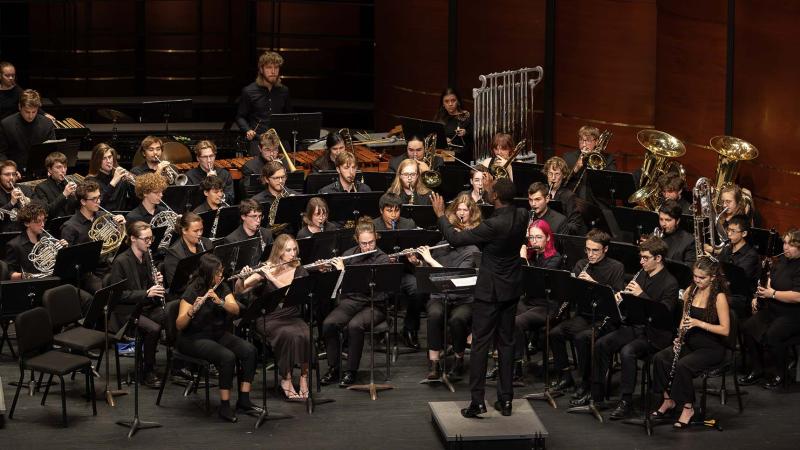 Wind Ensemble students and director dressed in concert black perform on the PAC stage