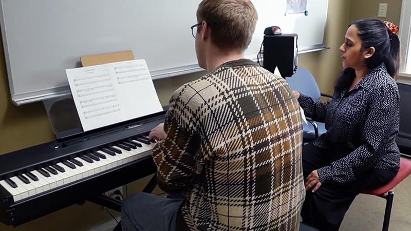 Asha Srinivathan, music composition faculty, with a student performing music at a keyboard
