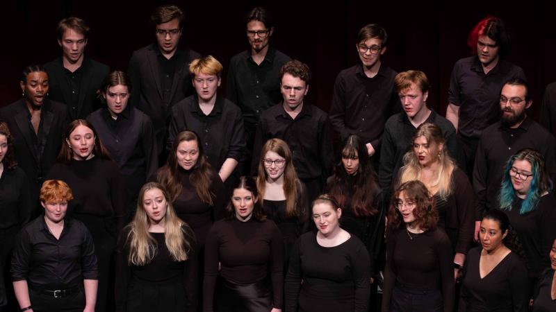 Vocalists in concert black sing on risers with their faces lit against the darkness of the auditorium