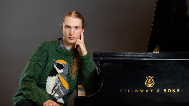 Kai Frueh poses next to a piano wearing a green bird sweater.