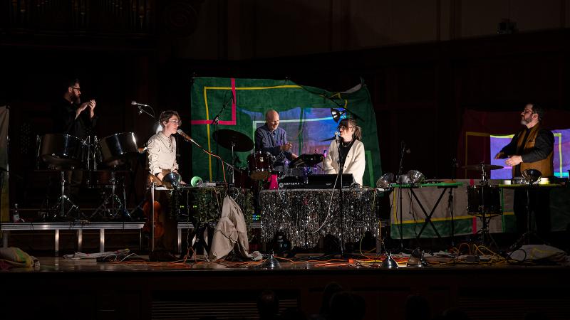 A small ensemble of percussionists and vocalists on a stage filled with instruments and props.