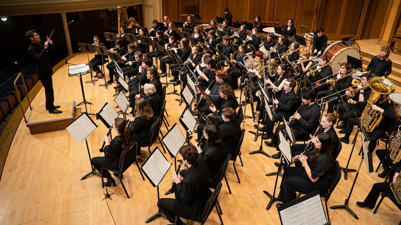 A large wind band led by a conductor.