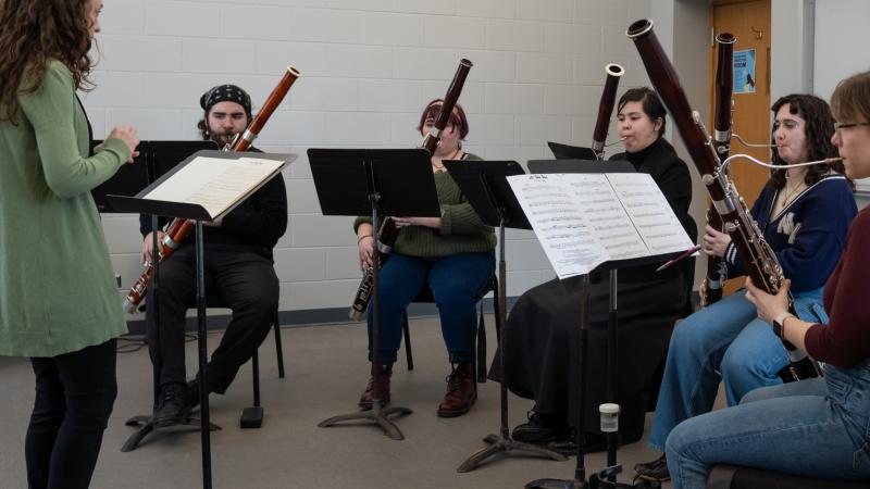 A conductor leading a small ensemble of musicians playing bassoons.