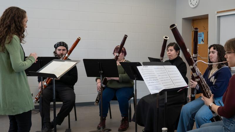 A conductor leading a small ensemble of musicians playing bassoons.