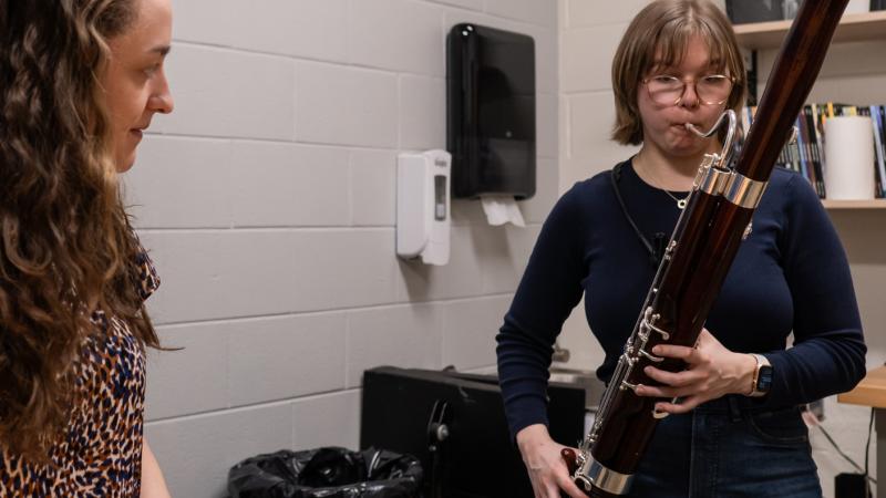 A teacher watches as a student plays bassoon.