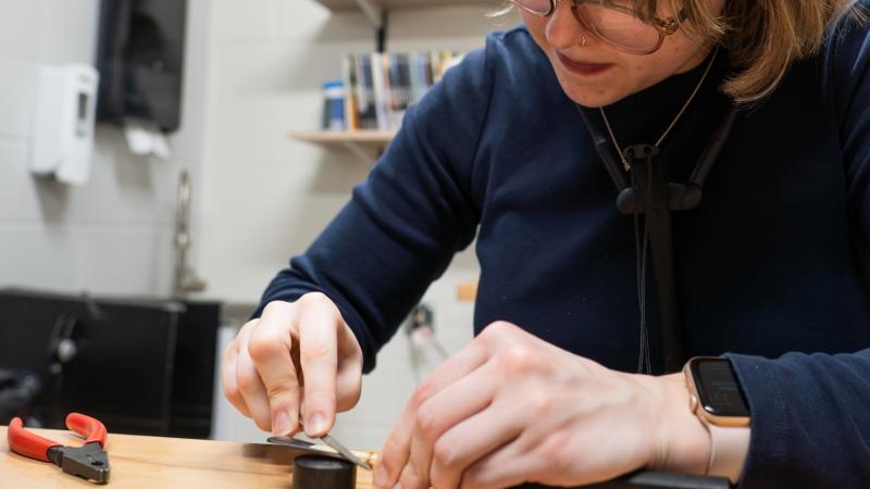 A student using tools to work on a bassoon reed.