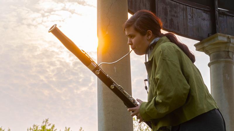 A musician playing bassoon in a gazebo outdoors.