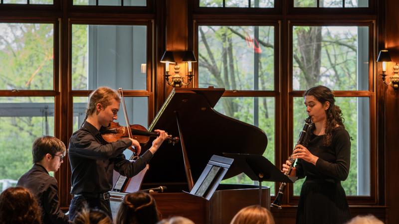 A trio of musicians playing violin, clarinet, and piano in performance.