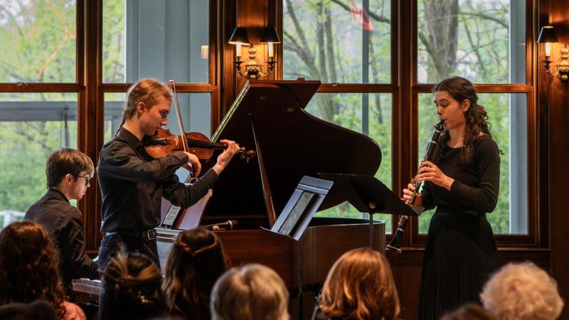 A trio of musicians playing violin, clarinet, and piano in performance.