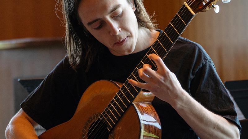 A student focused on playing acoustic guitar.