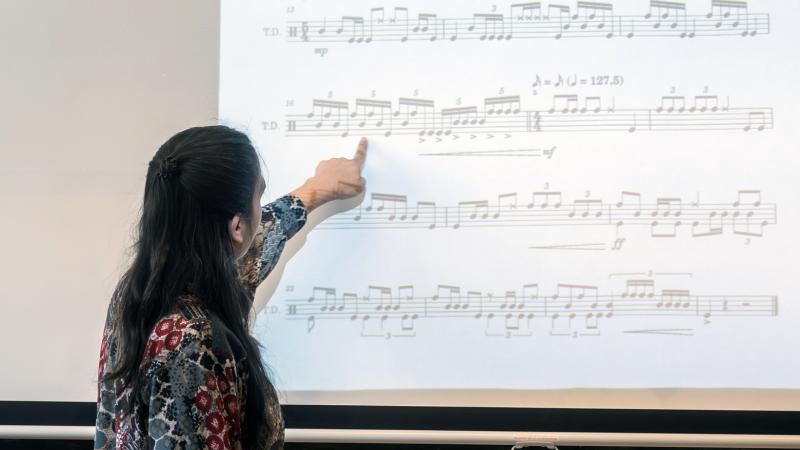 An instructor pointing at music notation on a projection screen.