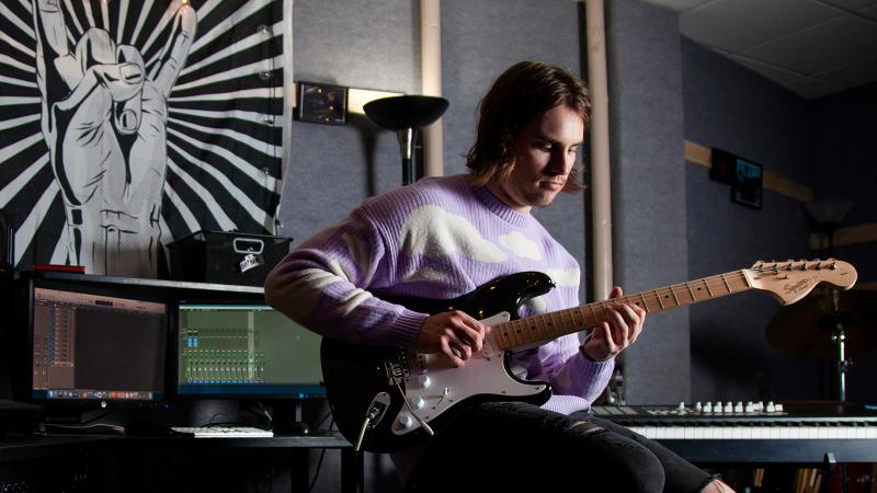 A musician playing electric guitar in an audio production studio.