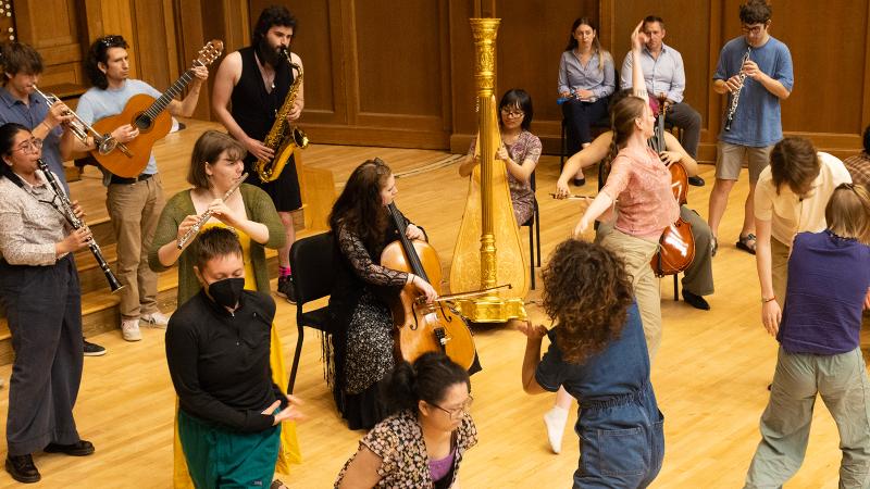 A group of musicians and dancers performing and moving about on stage.