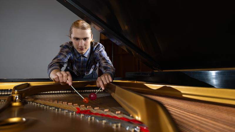 A musician playing on the strings of a piano with a pair of percussion mallets.