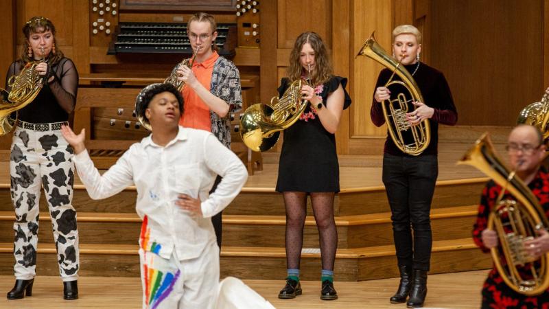 An ensemble of musicians playing horns and Wagner tubas, in collaboration with a dancer, in performance.