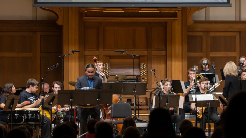 A large live screen projection of a steel pan over a jazz big band performing on stage.