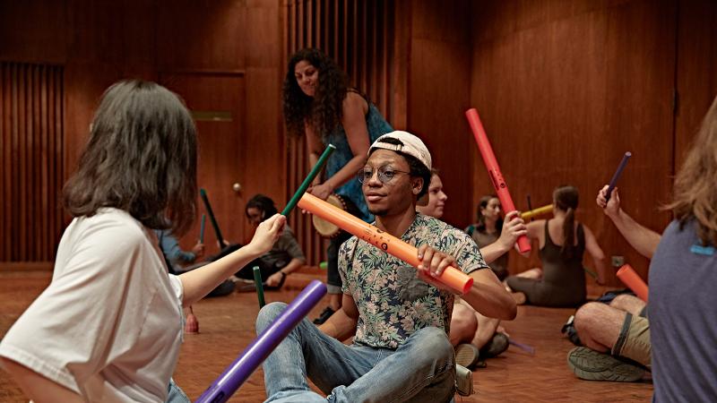 A large group of students playing with boomwhackers while seated on the floor.