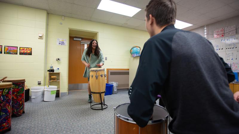 A student and a mentor-educator playing drums in a K-12 classroom.