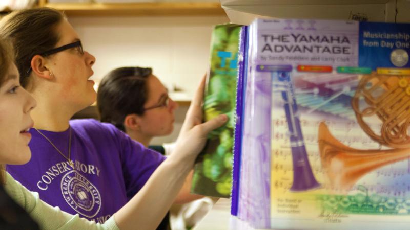 Students browsing through library shelves of teaching method books.