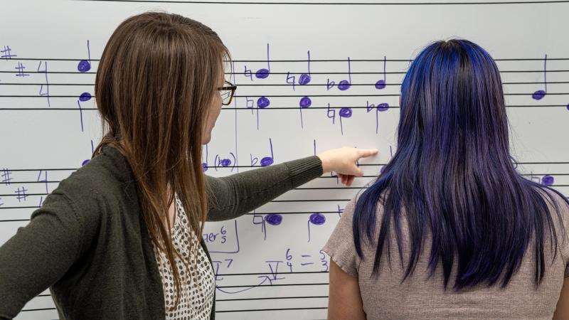 A teacher guides a student on part-writing on a whiteboard.