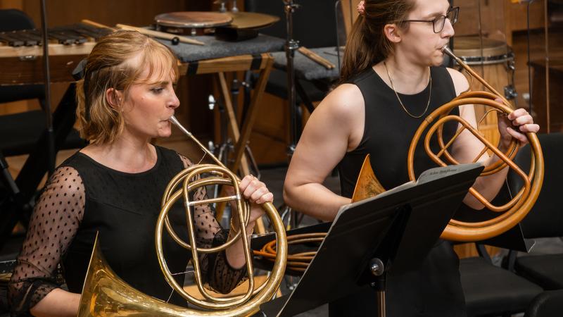 Two musicians playing natural horns in concert.