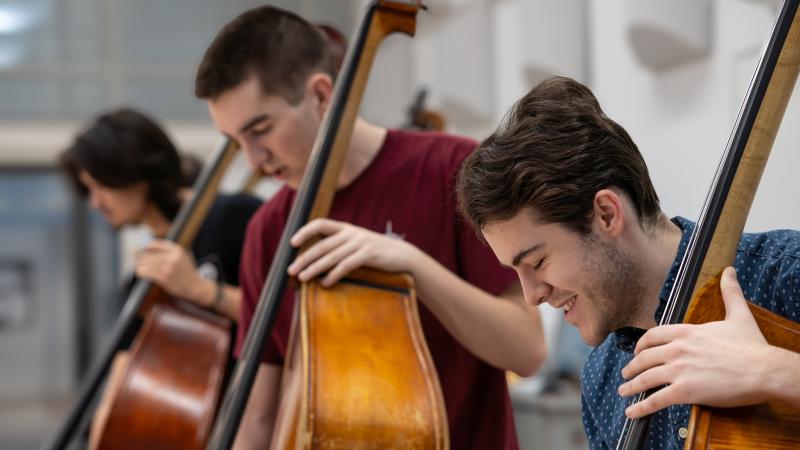 A small group of students playing upright basses in class.