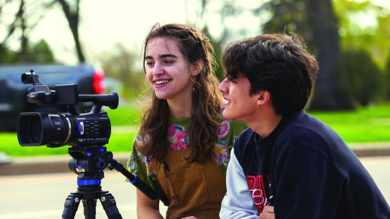 two students getting ready to film with grass and tree in the background