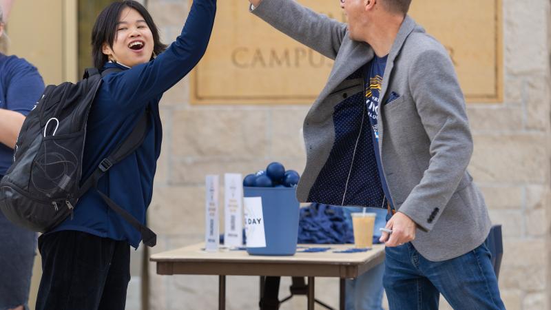 A student high fives a staff member after unlocking matching funds with a campus activity