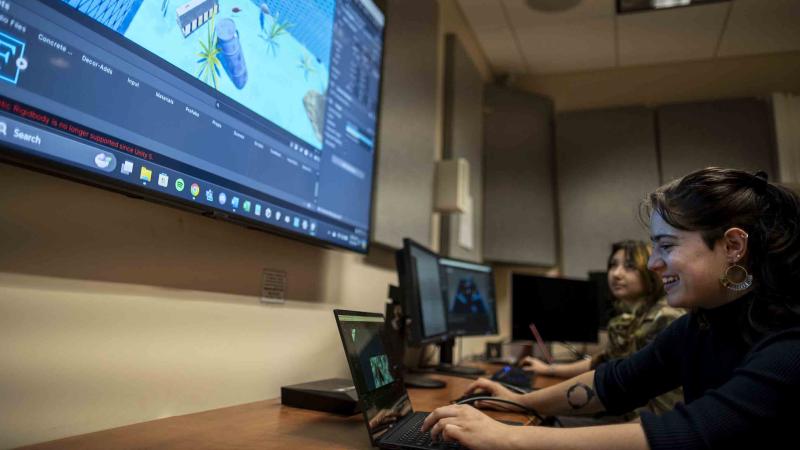 Student creating a video game world on a laptop while others watch on a big screen