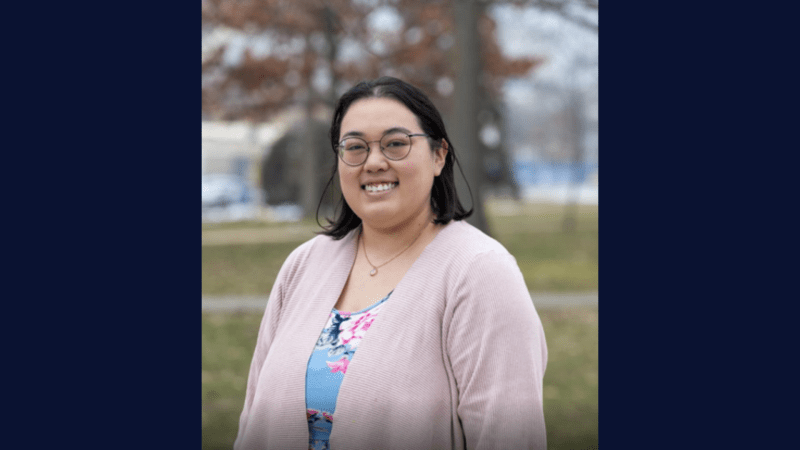 person wearing a pink and blue top, glasses and smiling for a photo outdoors