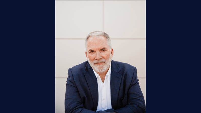 person wearing a white shirt and navy blue blazer in front of a white wall