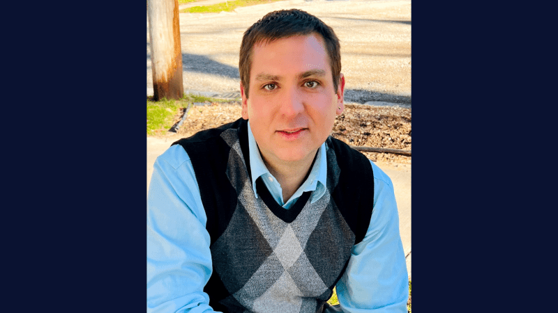 A person in a light blue shirt and multicolored vest