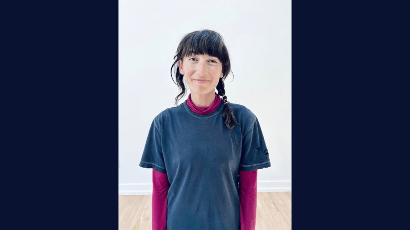 person standing in front of a white wall waring a blue and pink shirt and has long black hair